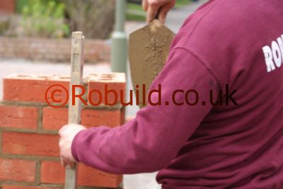 bricklayer using spirit level & brick trowel